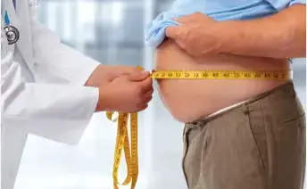 Doctor measuring a patient's waistline with a tape measure to evaluate clinical obesity risks